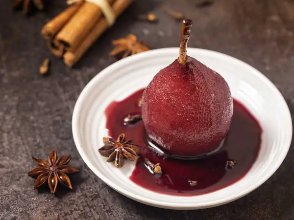 Peras al vino tinto, cocidas con especias como anís estrellado y canela, servidas en un plato blanco con su sirope.