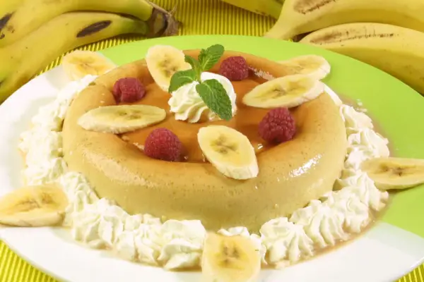 Delicioso flan de plátano adornado con rodajas de plátano, frambuesas y crema batida. Un postre perfecto para cualquier ocasión.