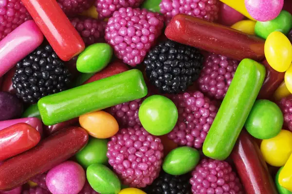Un surtido vibrante de chuches, mostrando cómo se hacen las chuches con formas de bayas, bastones y pastillas en tonos rojos, verdes, morados y amarillos.