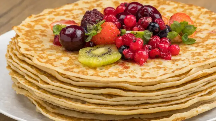 Pila de crepes dorados cubiertos con frutas rojas, fresas y kiwi. Una deliciosa receta crepes para disfrutar.